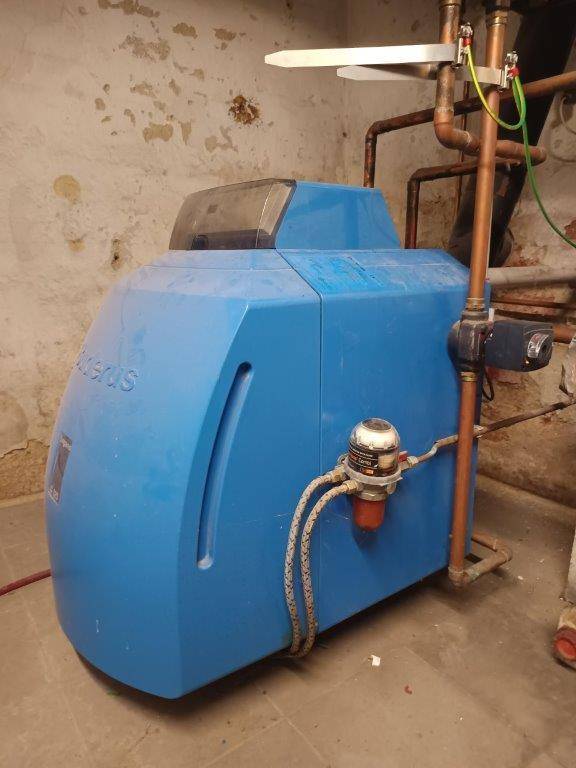 Detailansicht eines blauen Heizkessels mit Kupferrohren in einem Kellerraum.