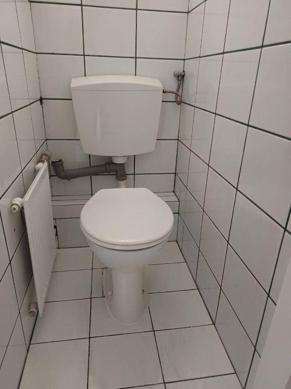 Separate Toilette mit weißen Fliesen und Heizkörper, funktional und sauber.