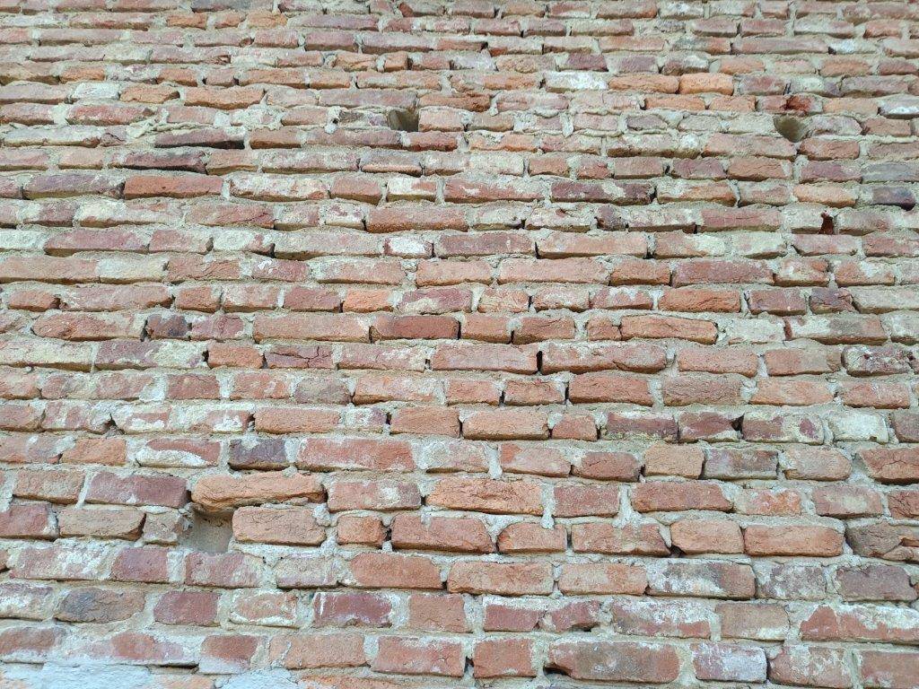 Nahaufnahme einer alten Ziegelmauer mit sichtbaren Fugen und leichten Beschädigungen, die den rustikalen Charme unterstreicht.