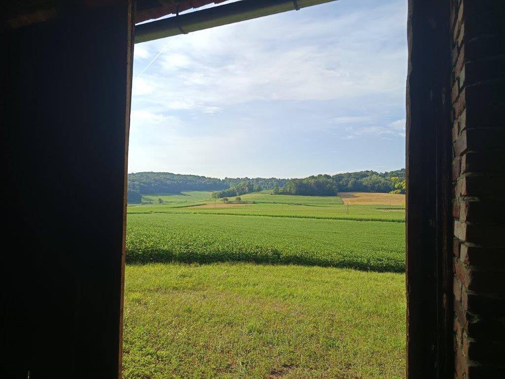 Weitläufiger Blick aus dem Gebäude auf eine grüne Landschaft mit Feldern und Wäldern unter blauem Himmel.