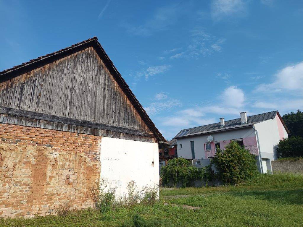 Altes Scheunengebäude mit Ziegelmauerwerk neben einem modernen Wohnhaus.