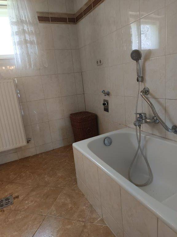 Badezimmer mit Badewanne, beigefarbenen Fliesen und einem Fenster für natürliche Belüftung.