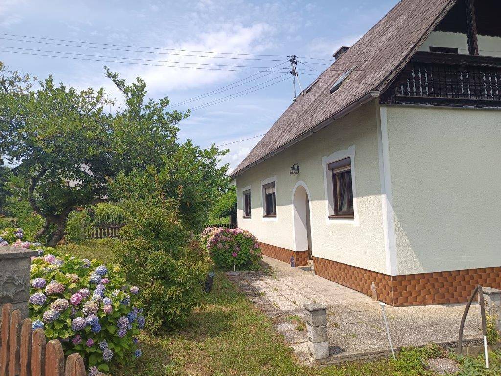Seitlicher Blick auf das Haus mit blühenden Hortensien im Vorgarten und gepflastertem Weg.