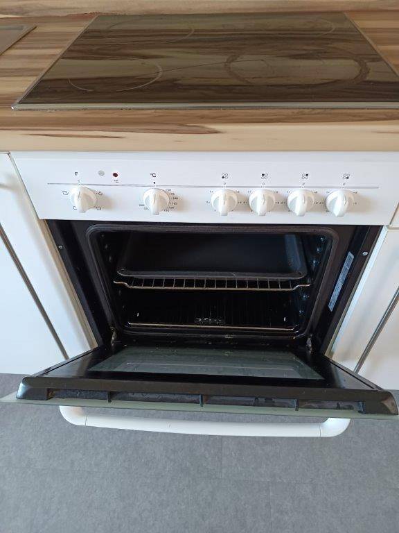 Eingebauter Backofen mit Cerankochfeld und Bedienknöpfen in einer Küche mit Holzoptik-Arbeitsplatte.