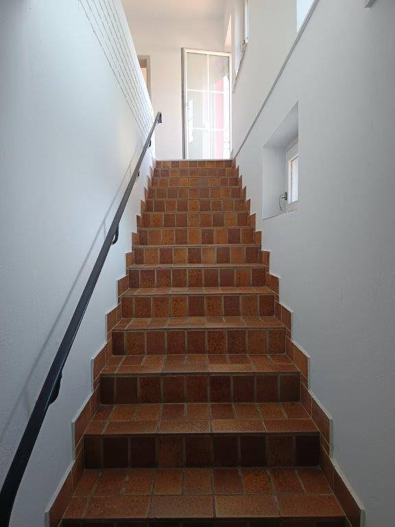 Treppenhaus mit Terrakotta-Fliesen und schwarzem Geländer, führt zu einem oberen Stockwerk.