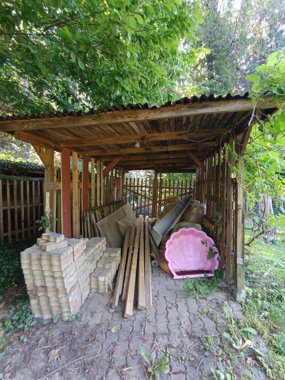 Rustikaler Holzschuppen im Garten, gefüllt mit Baumaterialien und Gartenutensilien.