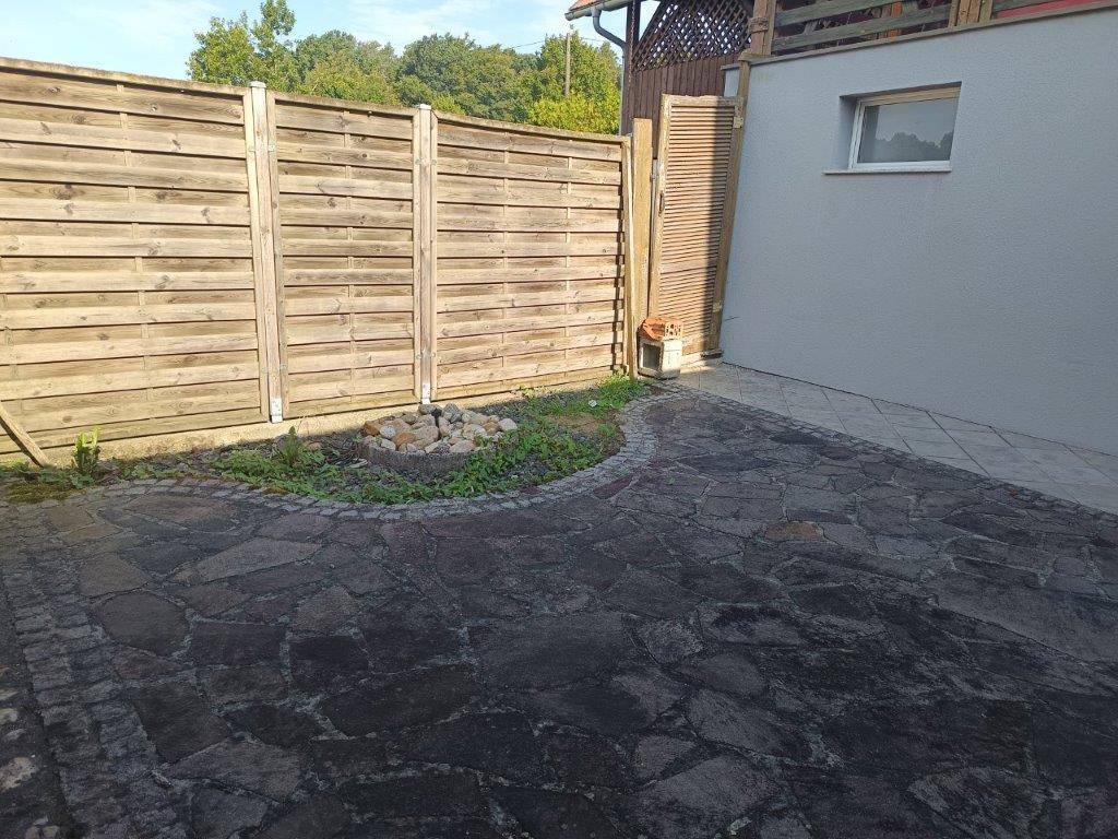 Geräumiger gepflasterter Patio mit Holzzaun und kleiner Feuerstelle im Freien.