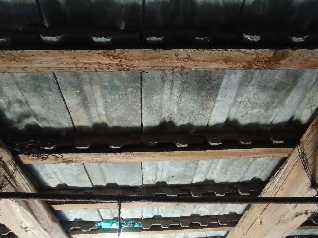 Nahaufnahme der Dachkonstruktion mit Holzbalken und der Unterseite von Wellblech- oder ähnlichen Dachplatten.