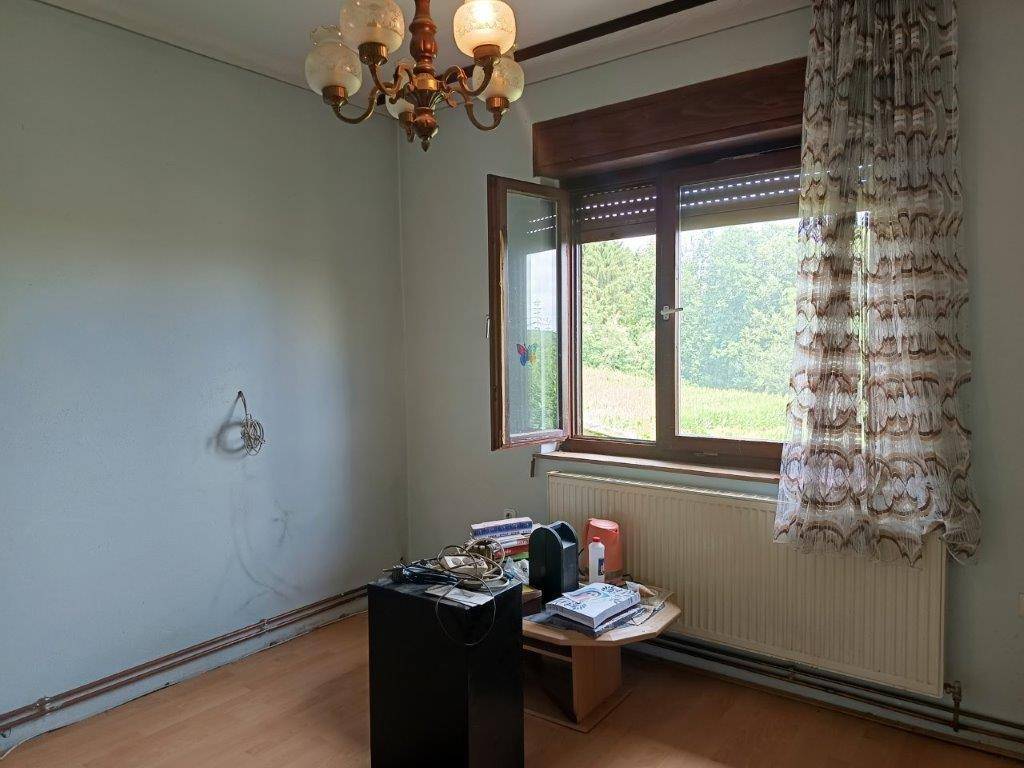 Zimmer mit Laminatboden, Fensterblick ins Grüne und einem traditionellen Kronleuchter.
