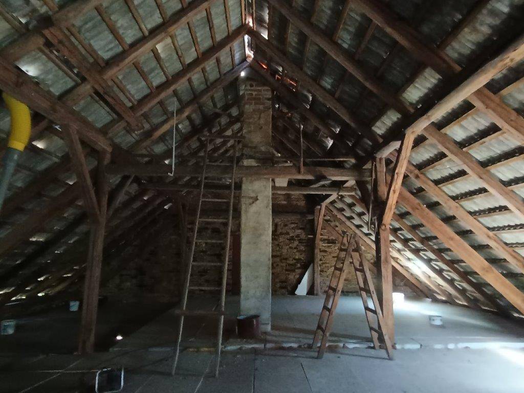 Unausgebauter Dachboden mit freiliegenden Holzbalken, einem gemauerten Kamin und mehreren Leitern.