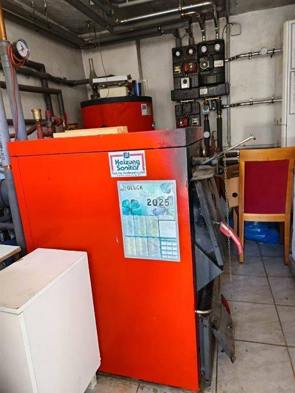 Rote Heizungsanlage mit Steuerungselementen und einem Kalender in einem Kellerraum.