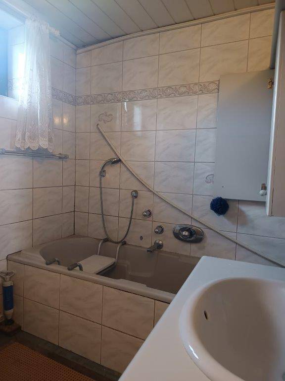 Badezimmer mit Badewanne, Waschbecken und Fliesen, in einem älteren Design.
