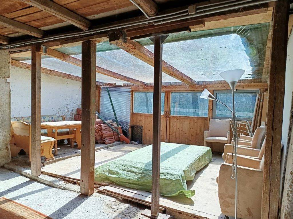 Unfertiger Wintergarten oder Anbau mit Holzbalken, Glasdach und provisorischer Einrichtung.
