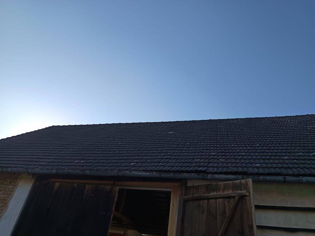 Blick auf das dunkle Ziegeldach der Scheune unter einem klaren, blauen Himmel.