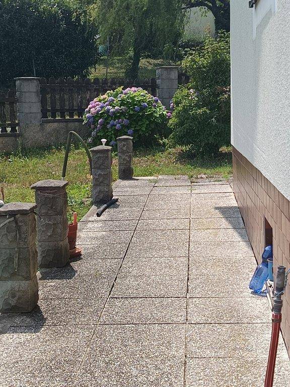 Gepflasterter Weg entlang der Hauswand mit blühenden Hortensien und Steinpfosten.