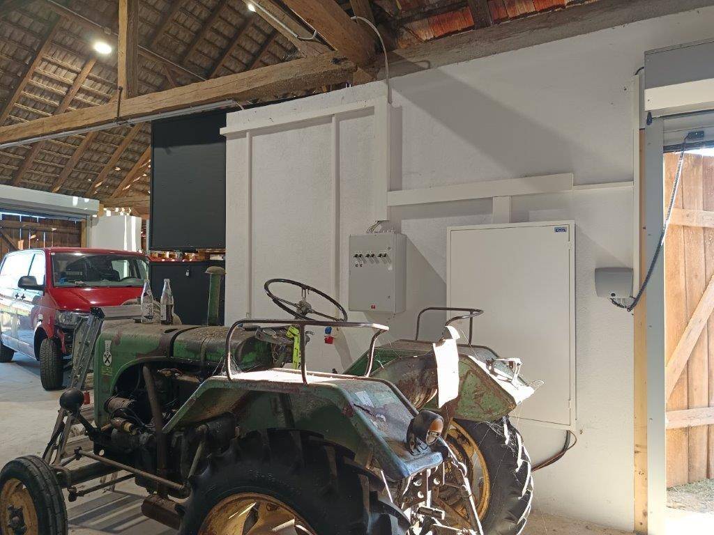 Geräumiger Innenraum der Scheune mit einem Traktor, einem roten Auto und sichtbaren elektrischen Installationen.