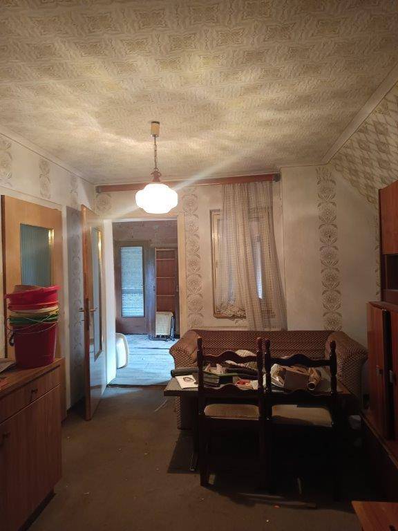 Wohnzimmer mit Sofa, Esstisch und traditioneller Einrichtung in einem älteren Gebäude.