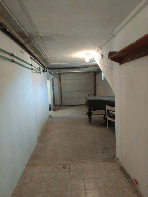 Geräumiger Kellerraum mit Betonboden, sichtbaren Rohren und Zugang zu einer Garage.