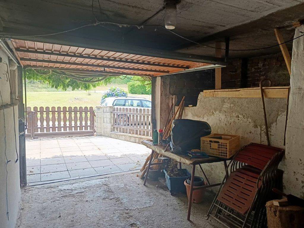 Offene Garage mit gepflastertem Vorplatz und Blick auf den Gartenbereich.