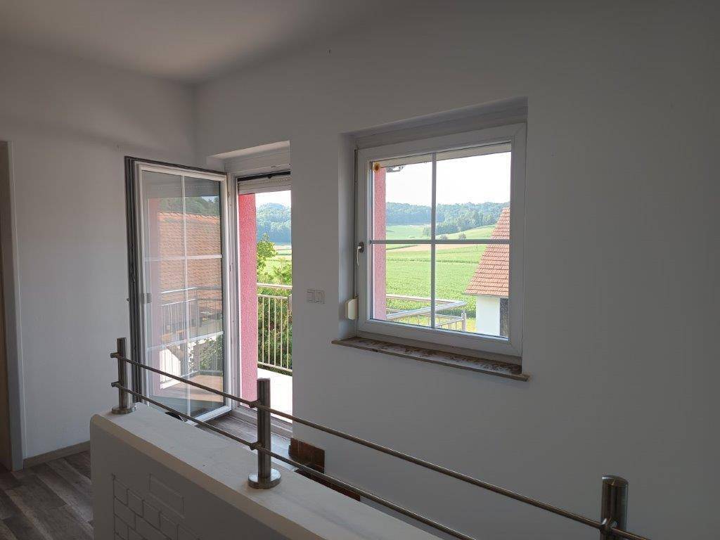 Heller Flur mit Fenster und französischem Balkon, bietet weiten Blick über Felder und Dächer.