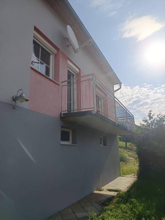 Seitenansicht des Hauses mit einem kleinen Balkon und Blick auf die grüne Umgebung.