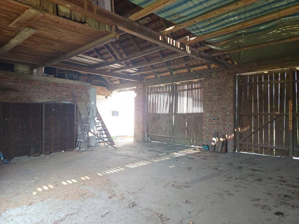 Geräumiger, ungenutzter Innenbereich mit rustikalen Holztüren und sichtbaren Ziegelwänden, ideal für Umbauprojekte.