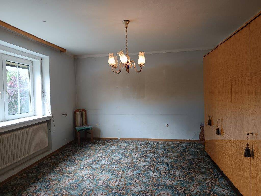 Schlafzimmer mit gemustertem Teppichboden, großem Kleiderschrank und einem Fenster für Tageslicht.