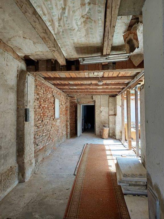 Langer Flur mit unverputzten Ziegelwänden, Holzbalkendecke und Teppichläufer.