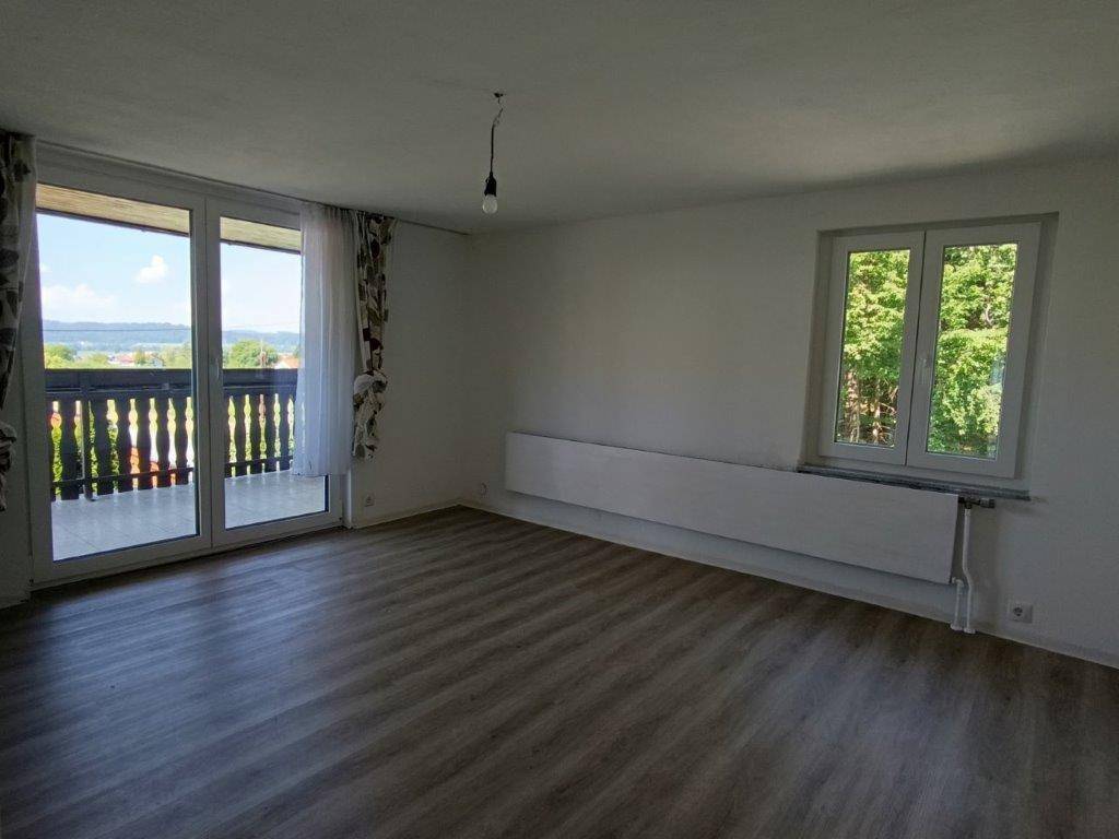 Geräumiges Wohnzimmer mit Balkonzugang, Laminatboden und einem Fenster mit Blick ins Grüne.