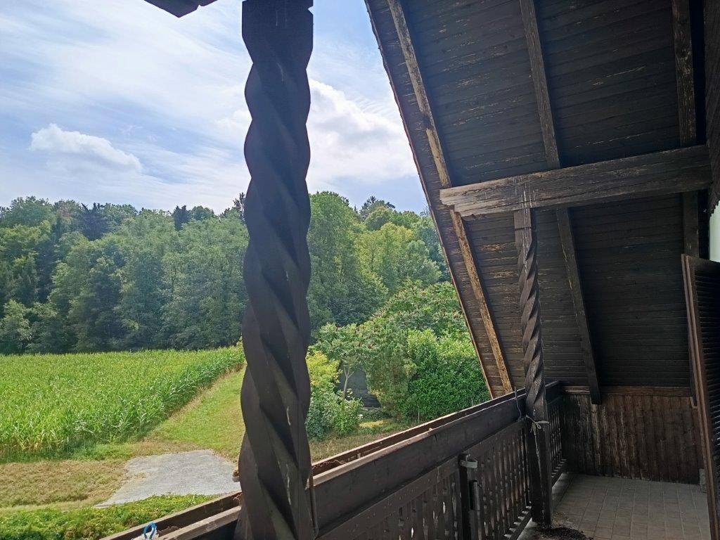 Detailansicht des Holzbalkons mit gedrechselter Säule und Blick auf ein Maisfeld.