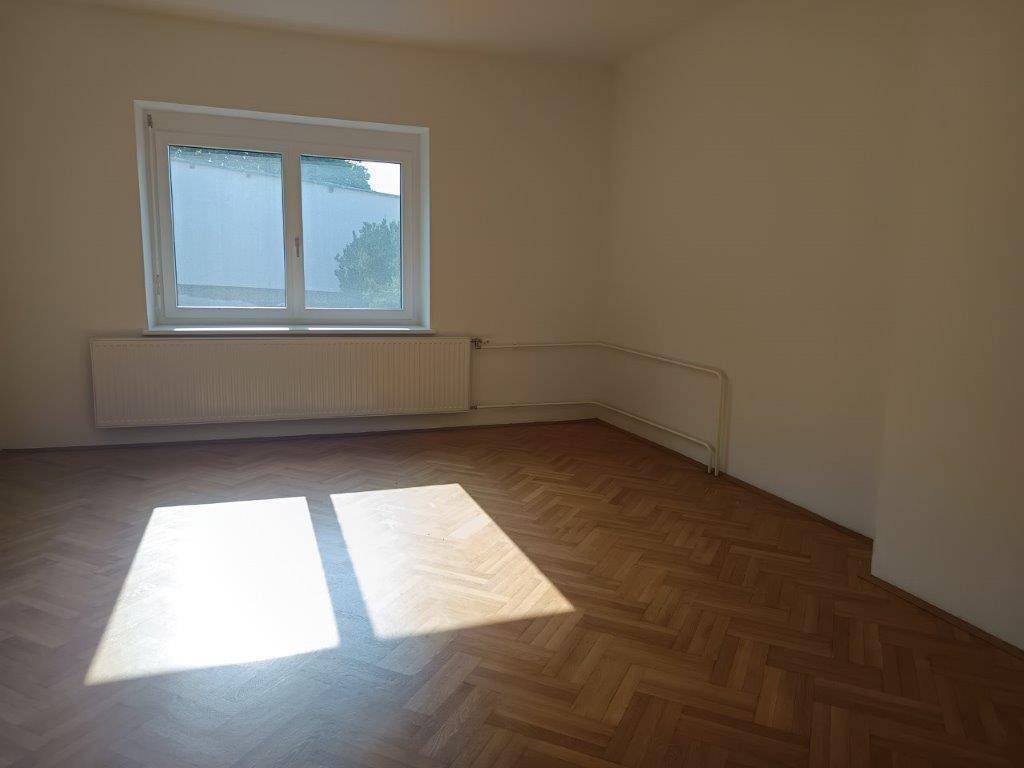 Sonniges Zimmer mit Parkettboden und Fenster, das viel natürliches Licht hereinlässt.