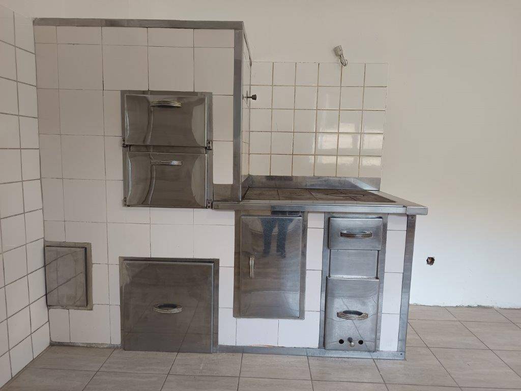 Detailansicht eines traditionellen Kachelofens mit Metalltüren und Fliesenverkleidung in der Küche.