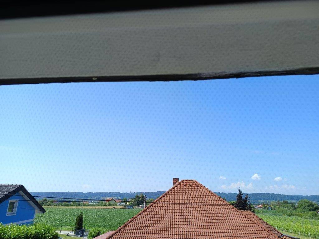 Weitblick über grüne Felder und Dächer von Häusern unter blauem Himmel, gesehen durch ein Fenster.