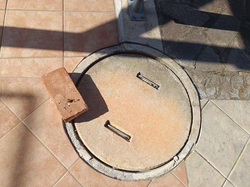 Runder Betondeckel auf einem gefliesten Außenbereich, möglicherweise ein Zugangsschacht.