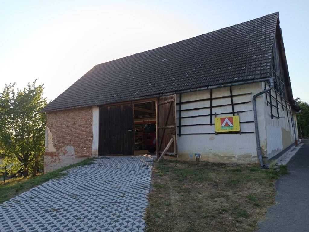 Eingangsbereich der Scheune mit gepflasterter Zufahrt und einem Immobilien-Werbeschild an der Fassade.