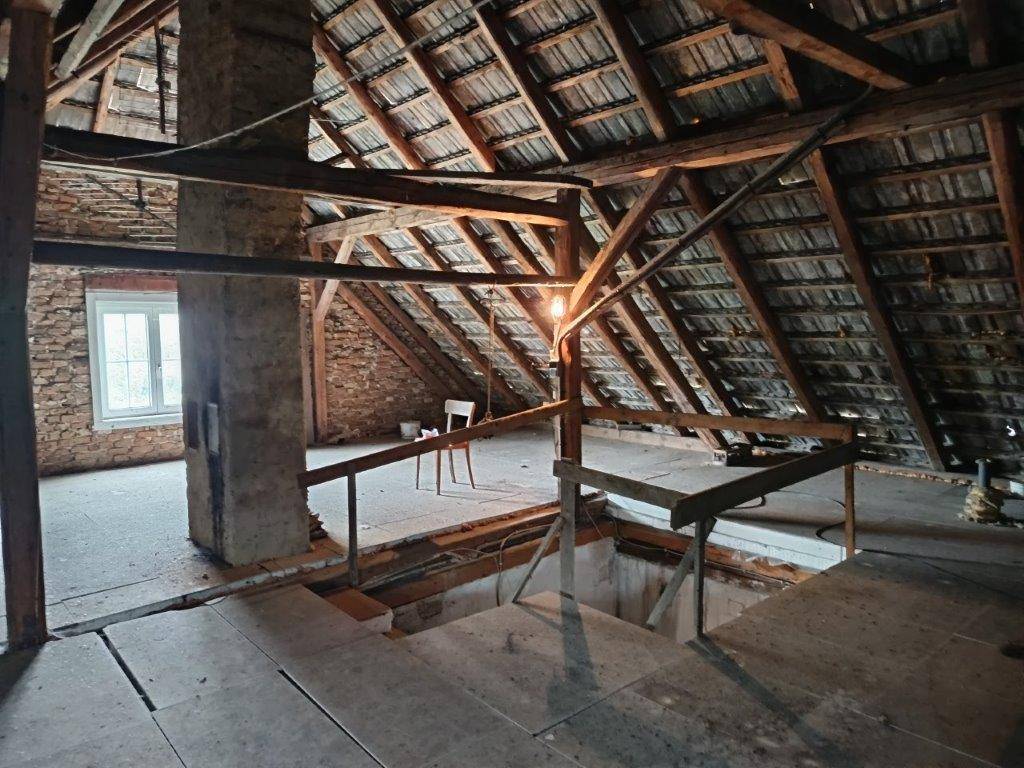 Großer Dachboden mit sichtbarer Holzkonstruktion, einem Fenster und einer Öffnung im Bodenbereich.