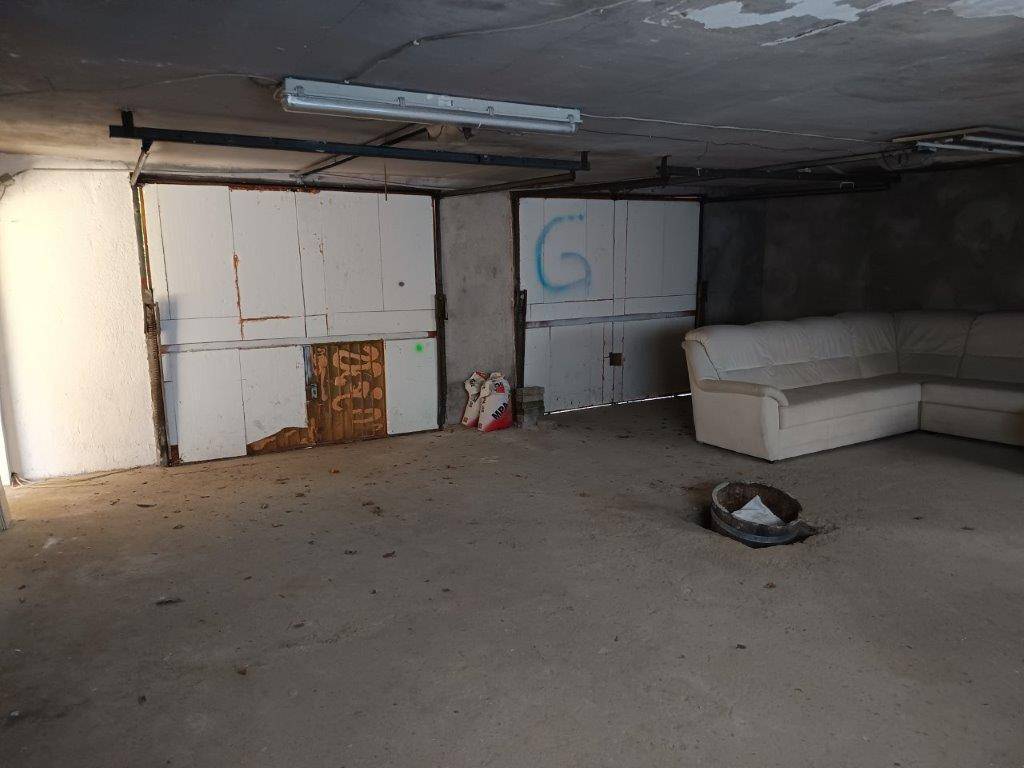 Großer Garagenraum im Keller mit zwei Toren, Betonboden und einer Couch.