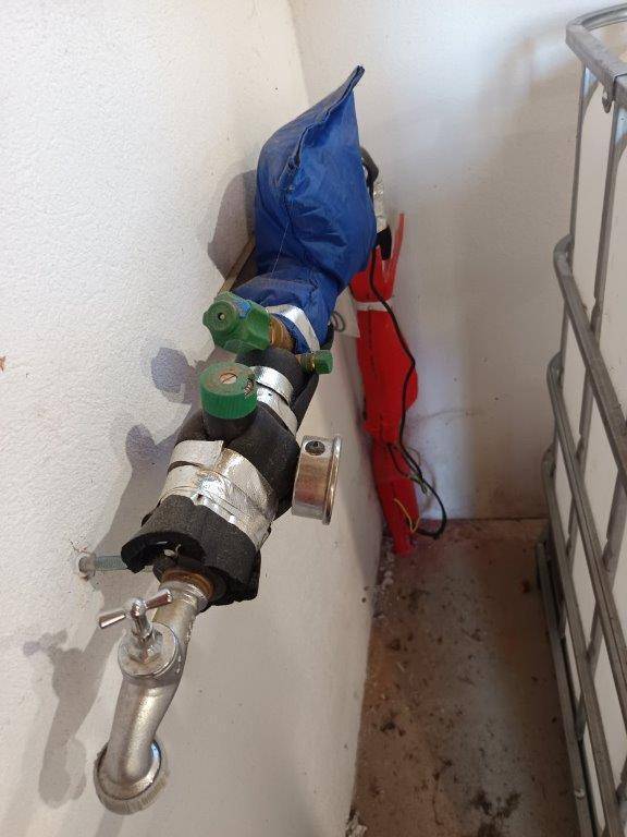 Wasserleitungen und ein Wasserhahn an der Wand, teilweise isoliert und geschützt.