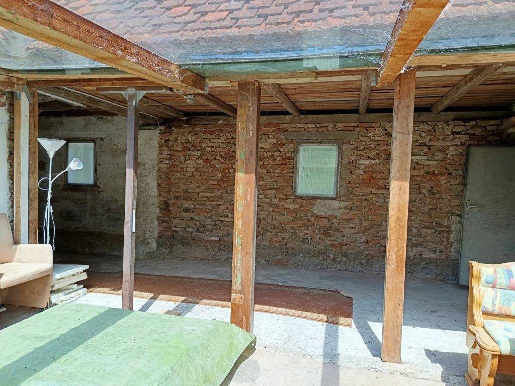 Rustikaler Anbau mit Holzbalken, Ziegelwänden und provisorischer Einrichtung, viel Tageslicht.