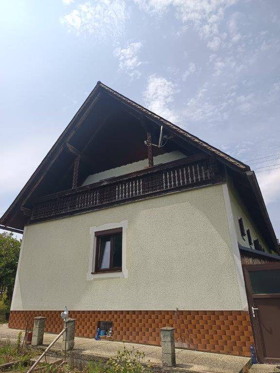 Seitenansicht des Hauses mit traditionellem Holzbalkon, Satteldach und einfacher Fassade.