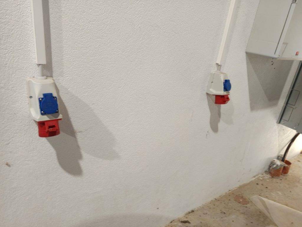 Weiße Wand im Innenbereich mit mehreren industriellen Steckdosen für Starkstromanschlüsse.