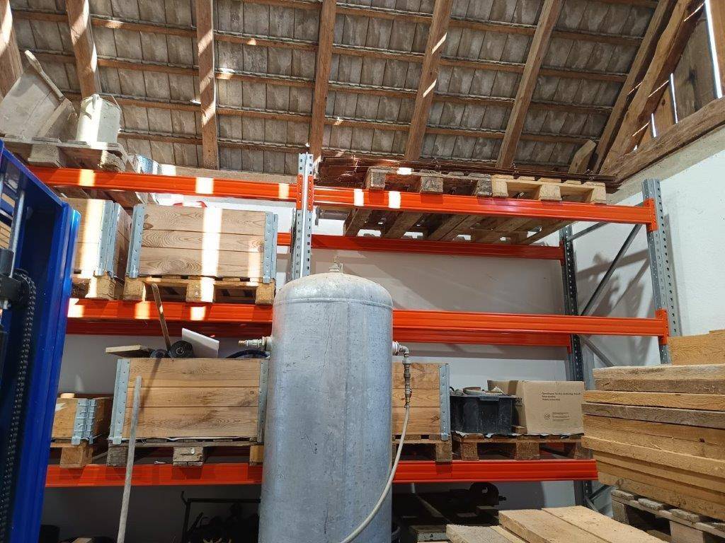 Lagerbereich in der Scheune mit stabilen Regalen, Holzpaletten und einem großen Metalltank.