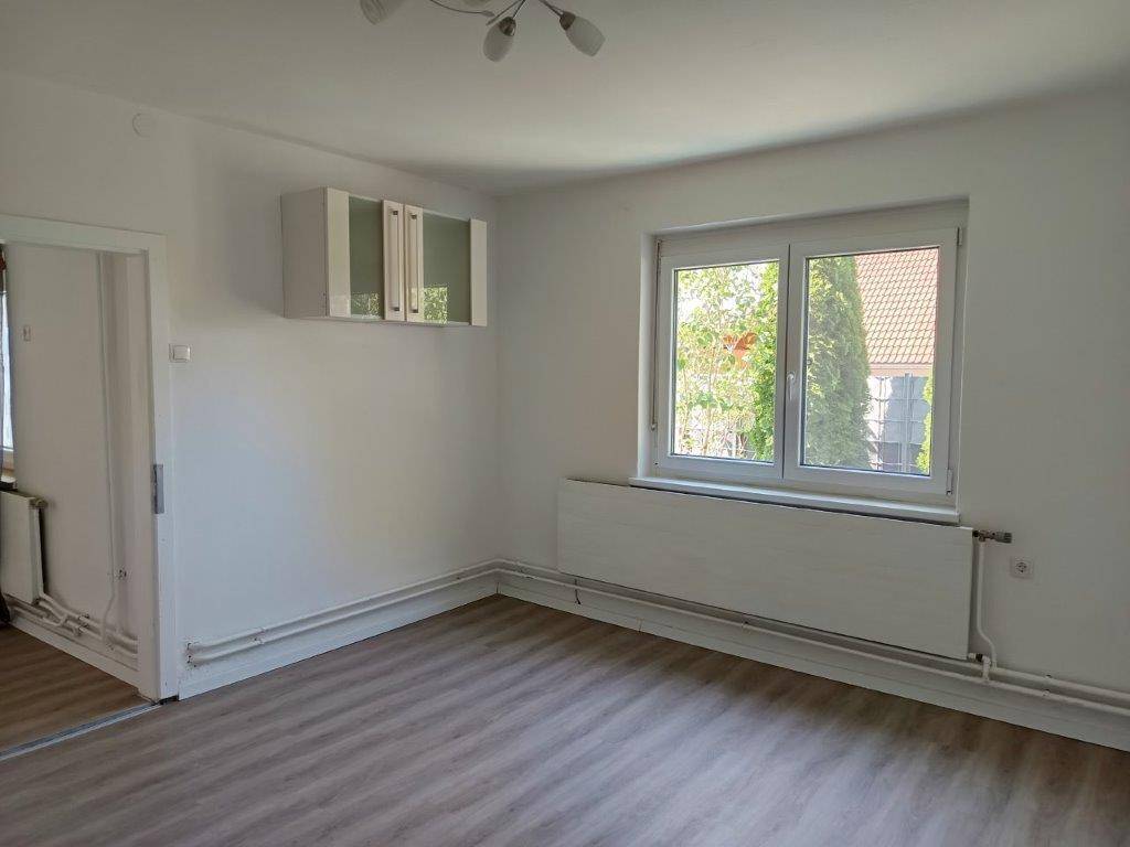 Helles Zimmer mit Laminatboden, weißen Wänden und einem Fenster mit Blick ins Grüne.