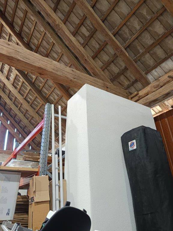Innenansicht der Scheune mit einer weißen Trennwand und der sichtbaren Holzdachkonstruktion.