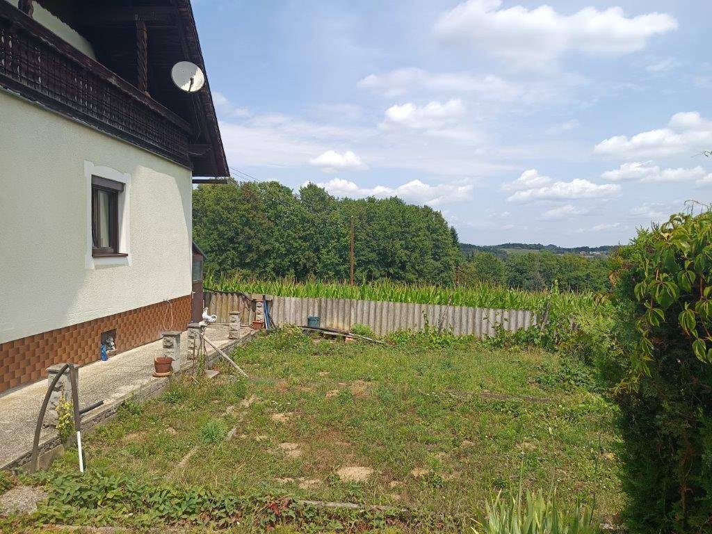 Hinterhof mit Rasenfläche und Blick auf weite Felder und bewaldete Hügel in der Ferne.