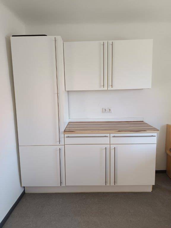 Kompakte Küchenzeile mit weißen Schränken und Holz-Arbeitsplatte, ideal für kleine Räume.
