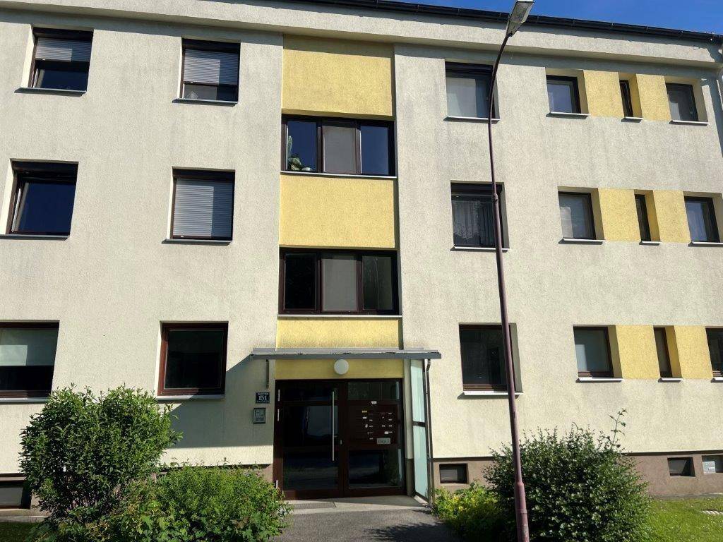 Mehrfamilienhaus mit gelber Fassade und mehreren Fenstern, umgeben von Grünflächen.