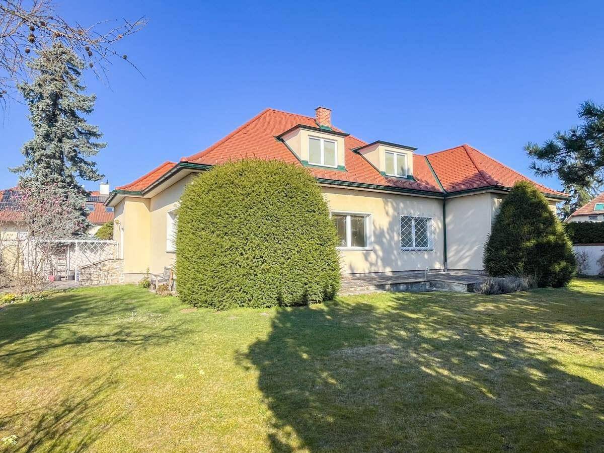 Großer, gepflegter Garten mit Rasenfläche und dem Haus im Hintergrund unter blauem Himmel.