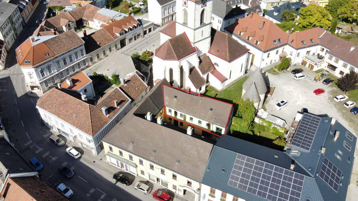 Luftaufnahme eines historischen Stadtzentrums mit einem markierten Gebäude und umliegenden Dächern.
