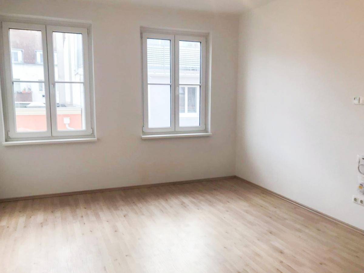 Ein lichtdurchfluteter Raum mit zwei Fenstern und hellem Laminatboden, ideal für Wohn- oder Schlafzimmer.